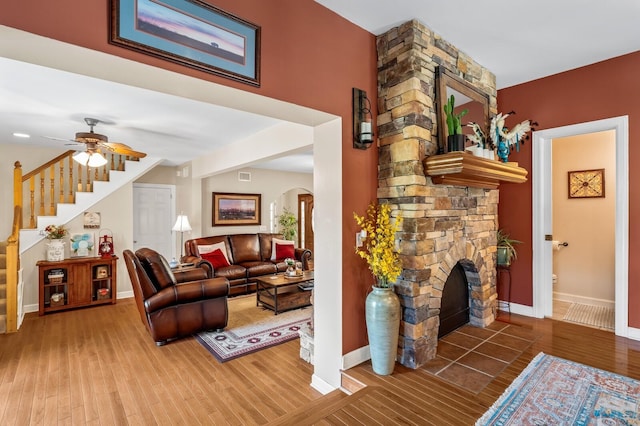 living room with hardwood / wood-style floors, a stone fireplace, and ceiling fan