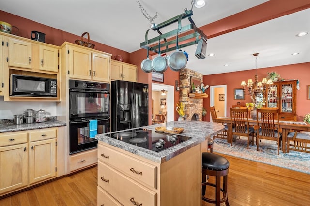 kitchen featuring a kitchen breakfast bar, black appliances, light hardwood / wood-style flooring, a kitchen island, and hanging light fixtures