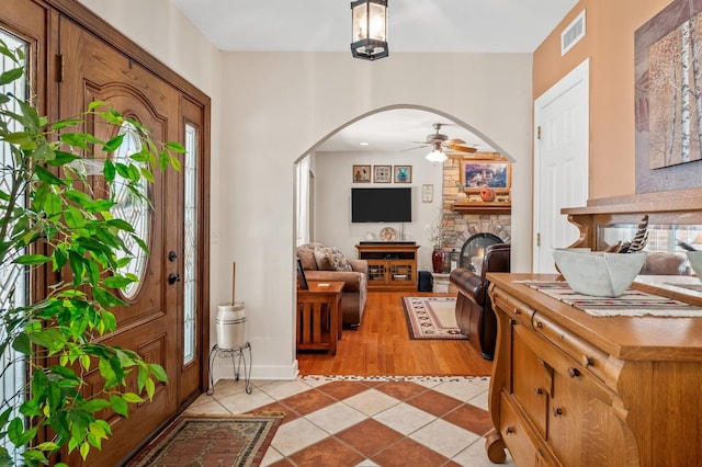 tiled entryway with ceiling fan, a stone fireplace, and a wealth of natural light