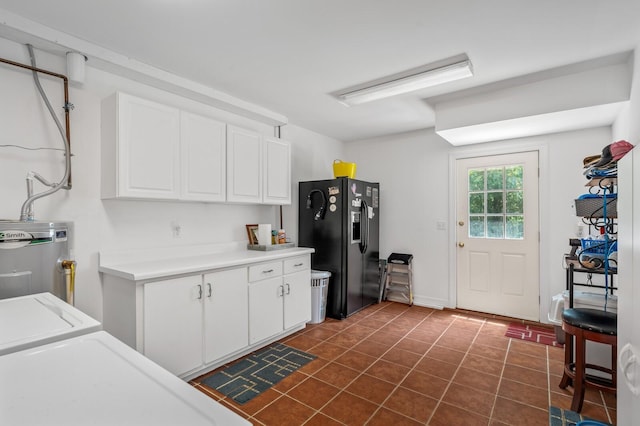 kitchen featuring black fridge with ice dispenser, water heater, dark tile patterned flooring, washing machine and clothes dryer, and white cabinetry