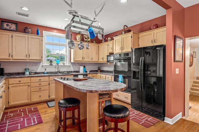 kitchen featuring a breakfast bar area, a kitchen island, black appliances, and light wood-type flooring