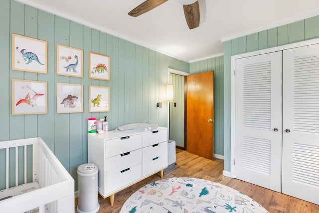 bedroom with wooden walls, ceiling fan, ornamental molding, light hardwood / wood-style floors, and a closet