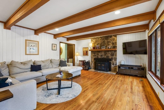 living room with wood walls, beam ceiling, a stone fireplace, and light hardwood / wood-style flooring