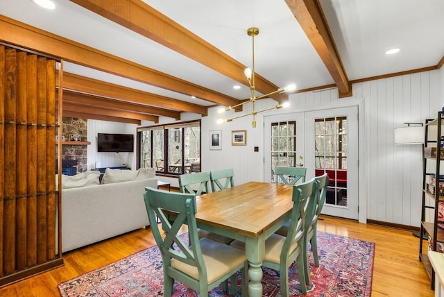 dining space with french doors, wooden walls, light hardwood / wood-style floors, a fireplace, and beam ceiling