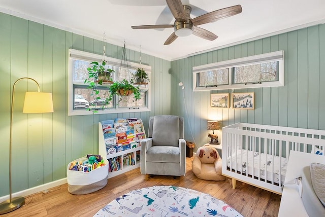 bedroom featuring ceiling fan, wood-type flooring, a crib, and multiple windows