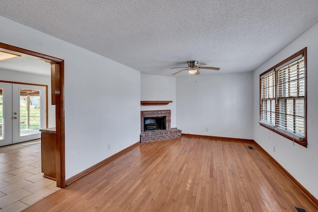 unfurnished living room featuring ceiling fan, french doors, a brick fireplace, a textured ceiling, and light wood-type flooring