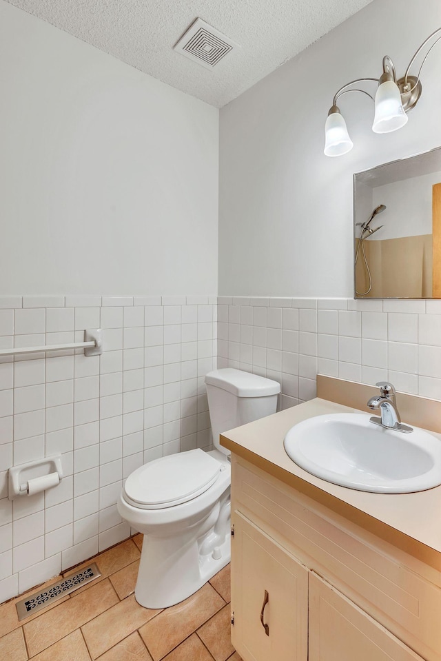 bathroom featuring vanity, a textured ceiling, tile walls, tile patterned flooring, and toilet