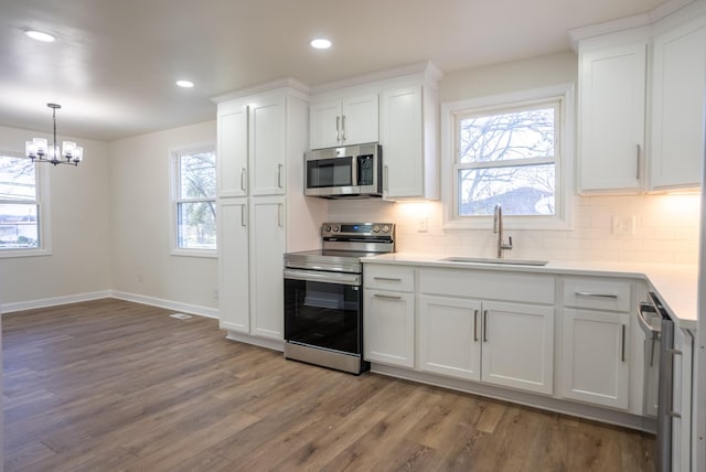 kitchen featuring sink, hardwood / wood-style flooring, white cabinetry, stainless steel appliances, and a chandelier