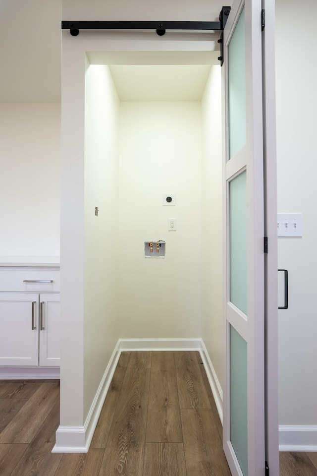 washroom with electric dryer hookup, a barn door, hookup for a washing machine, and dark wood-type flooring