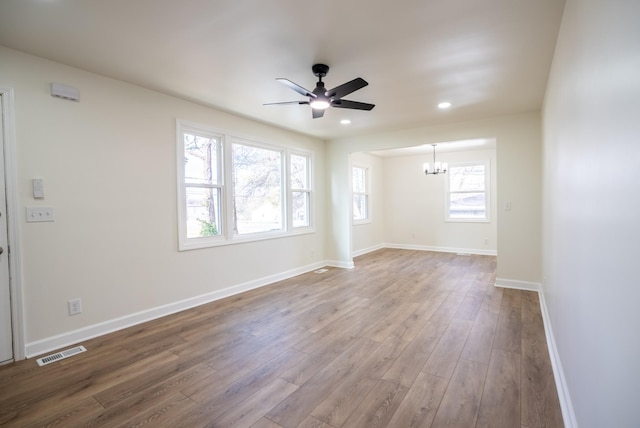 unfurnished room featuring plenty of natural light, wood-type flooring, and ceiling fan with notable chandelier