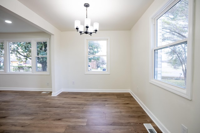 unfurnished dining area with a healthy amount of sunlight, dark wood-type flooring, and a notable chandelier