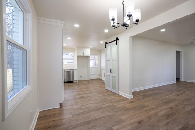 unfurnished dining area featuring a barn door, wood-type flooring, and an inviting chandelier