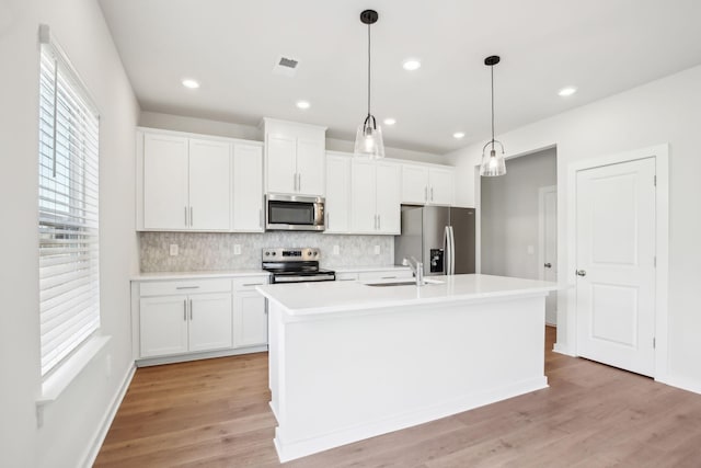 kitchen featuring an island with sink, white cabinetry, appliances with stainless steel finishes, and light countertops