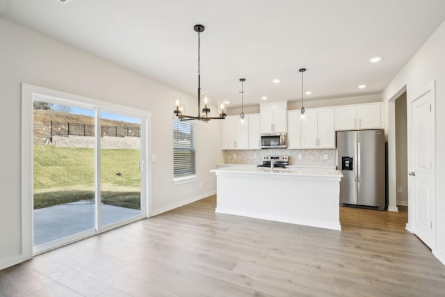 kitchen with stainless steel appliances, white cabinets, hanging light fixtures, light countertops, and an island with sink