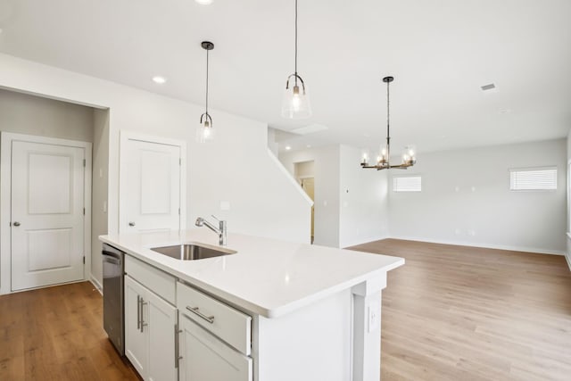 kitchen featuring a kitchen island with sink, a sink, light countertops, dishwasher, and decorative light fixtures