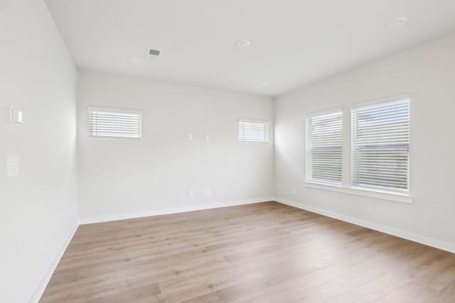 spare room featuring light wood-type flooring, visible vents, and baseboards