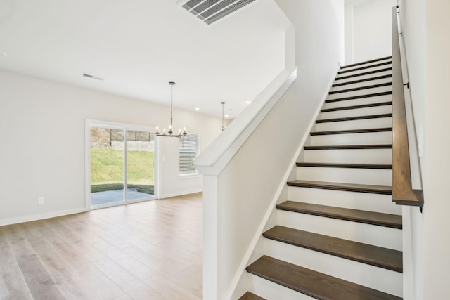 stairway with visible vents, a notable chandelier, baseboards, and wood finished floors