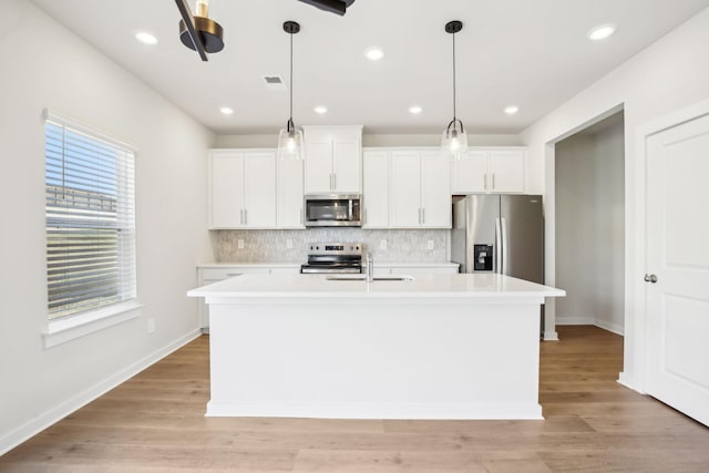 kitchen with stainless steel appliances, a sink, white cabinetry, light countertops, and a center island with sink