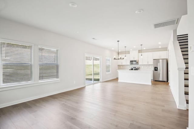 unfurnished living room with baseboards, visible vents, an inviting chandelier, stairs, and light wood-style floors