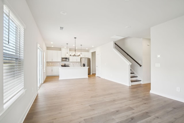 unfurnished living room featuring light wood-style floors, visible vents, stairway, and a notable chandelier