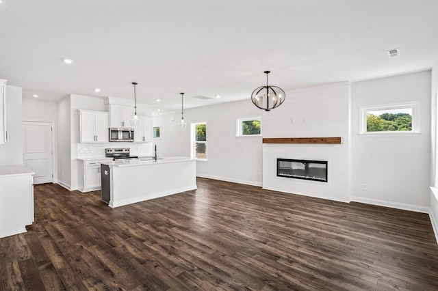 kitchen with pendant lighting, white cabinets, a fireplace, an island with sink, and stainless steel appliances