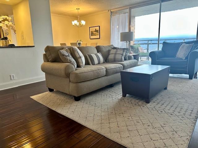 living room with a textured ceiling, dark wood-type flooring, crown molding, and an inviting chandelier