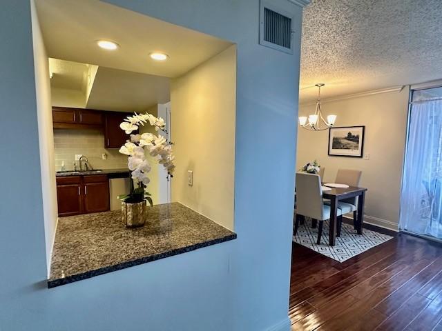 kitchen with decorative backsplash, dark hardwood / wood-style flooring, dark stone counters, a textured ceiling, and decorative light fixtures