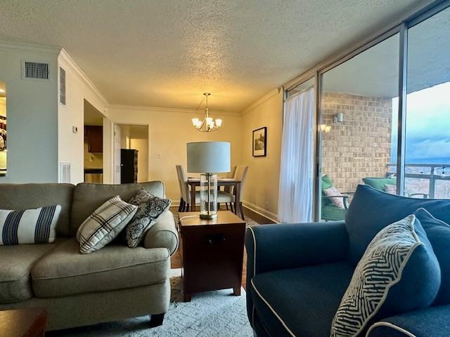 living room featuring carpet flooring, crown molding, a textured ceiling, and a notable chandelier