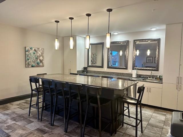 bar with sink, decorative light fixtures, white cabinetry, and dark stone countertops