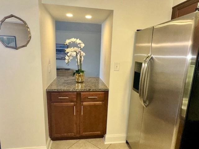 kitchen featuring stainless steel fridge with ice dispenser, light tile patterned floors, and dark stone counters