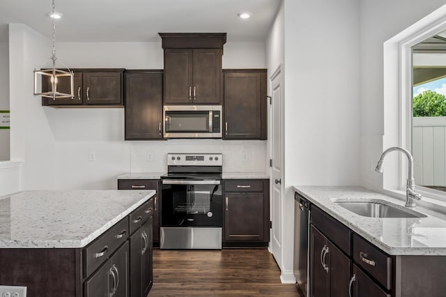 kitchen featuring pendant lighting, sink, light stone countertops, appliances with stainless steel finishes, and dark brown cabinets