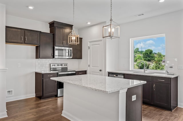 kitchen featuring dark wood-type flooring, sink, appliances with stainless steel finishes, decorative light fixtures, and a kitchen island