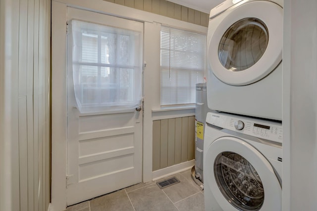 laundry area featuring wood walls, stacked washing maching and dryer, water heater, and light tile patterned flooring