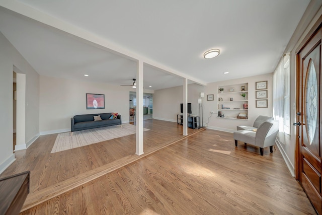 unfurnished room with wood-type flooring, built in shelves, and ceiling fan