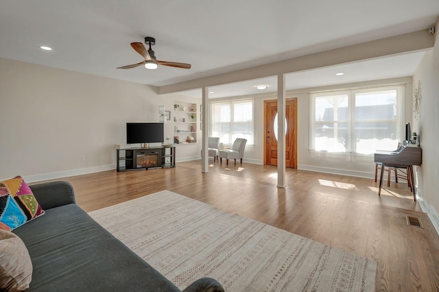 living room featuring built in features, light wood-type flooring, and ceiling fan