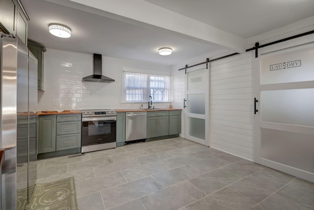 kitchen with appliances with stainless steel finishes, wood counters, wall chimney range hood, sink, and a barn door