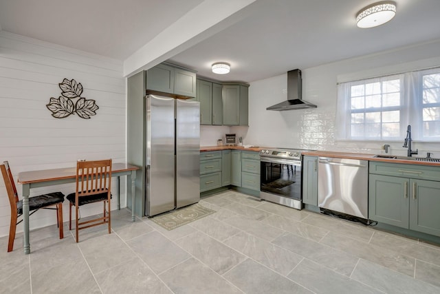 kitchen with appliances with stainless steel finishes, sink, wall chimney range hood, green cabinetry, and wood counters