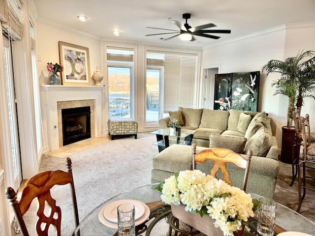 living room featuring a tiled fireplace, carpet floors, ornamental molding, and ceiling fan