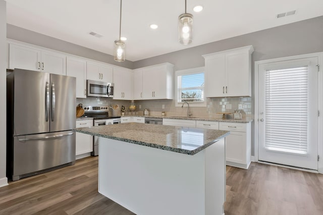 kitchen featuring sink, appliances with stainless steel finishes, white cabinetry, a kitchen island, and decorative light fixtures