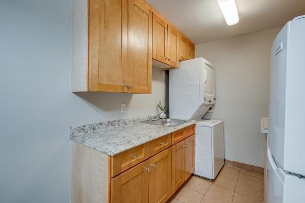 clothes washing area featuring sink, light tile patterned floors, cabinets, and stacked washer / drying machine