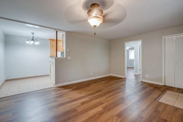 spare room featuring ceiling fan with notable chandelier and light wood-type flooring