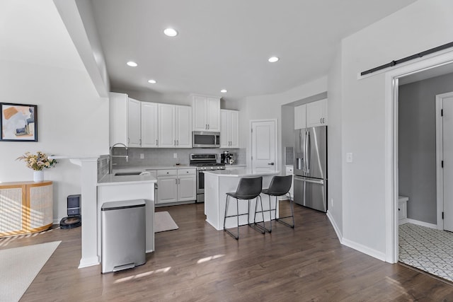 kitchen with white cabinetry, stainless steel appliances, a kitchen breakfast bar, a barn door, and backsplash