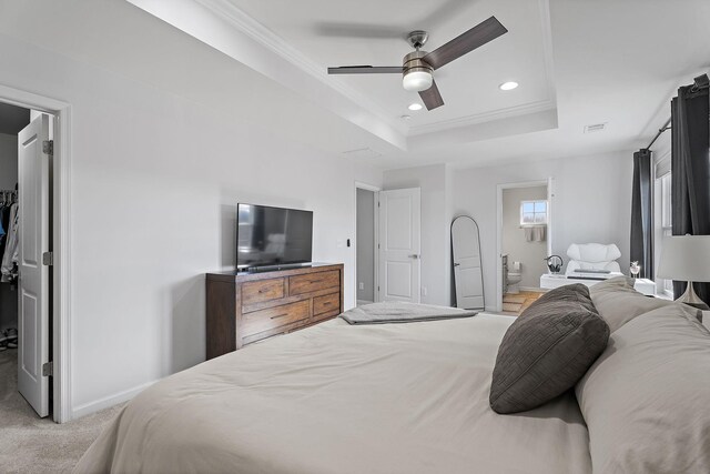 carpeted bedroom with a tray ceiling, ensuite bathroom, crown molding, and ceiling fan