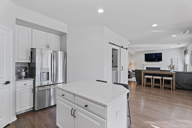 kitchen with decorative backsplash, a kitchen island, a barn door, stainless steel fridge with ice dispenser, and white cabinetry