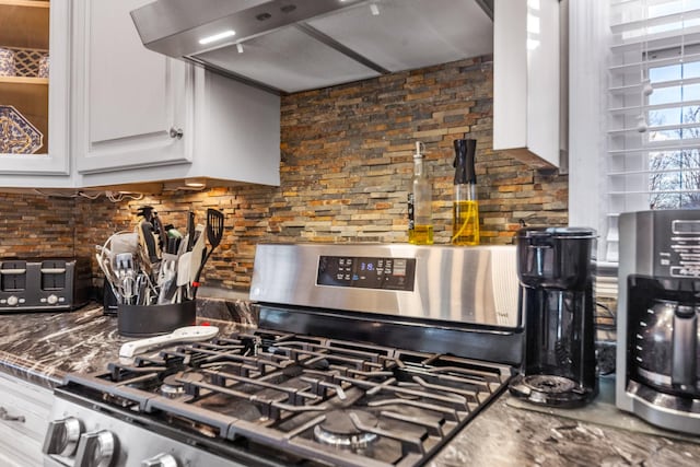 interior details with dark stone counters, white cabinets, tasteful backsplash, gas stove, and extractor fan