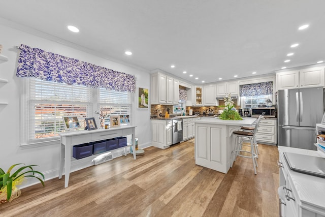 kitchen with a kitchen breakfast bar, white cabinets, decorative backsplash, a kitchen island, and appliances with stainless steel finishes