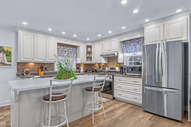 kitchen featuring stainless steel appliances, light hardwood / wood-style flooring, decorative backsplash, a breakfast bar, and white cabinets