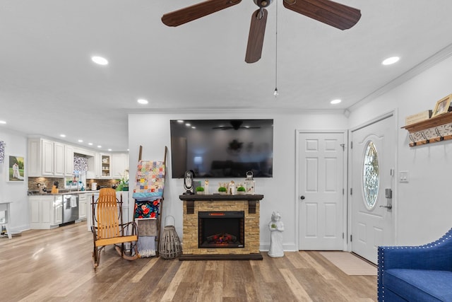 living room with a fireplace, light hardwood / wood-style floors, ceiling fan, and crown molding