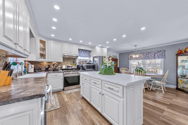 kitchen featuring a center island, backsplash, white cabinets, decorative light fixtures, and stainless steel appliances