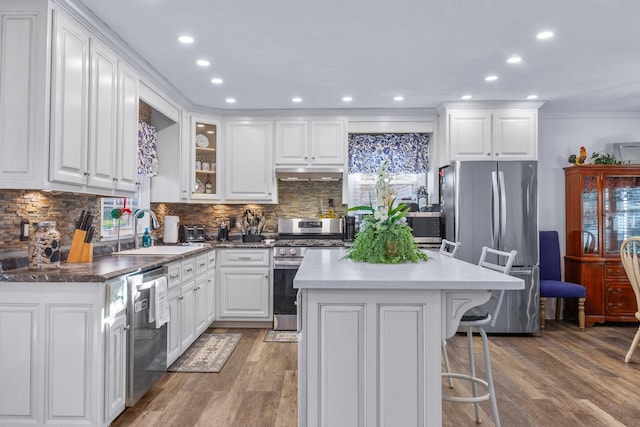 kitchen featuring hardwood / wood-style floors, white cabinets, a kitchen breakfast bar, sink, and appliances with stainless steel finishes